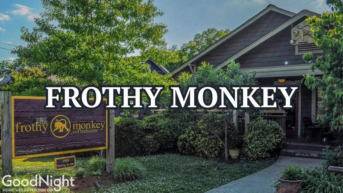 The exterior of the Frothy Monkey coffeehouse is shown, with friendly signage, a welcoming entrance, and greenery around the seating area. The atmosphere is relaxed and inviting, suggesting a perfect spot to start the day with coffee or enjoy a casual break during city adventures.