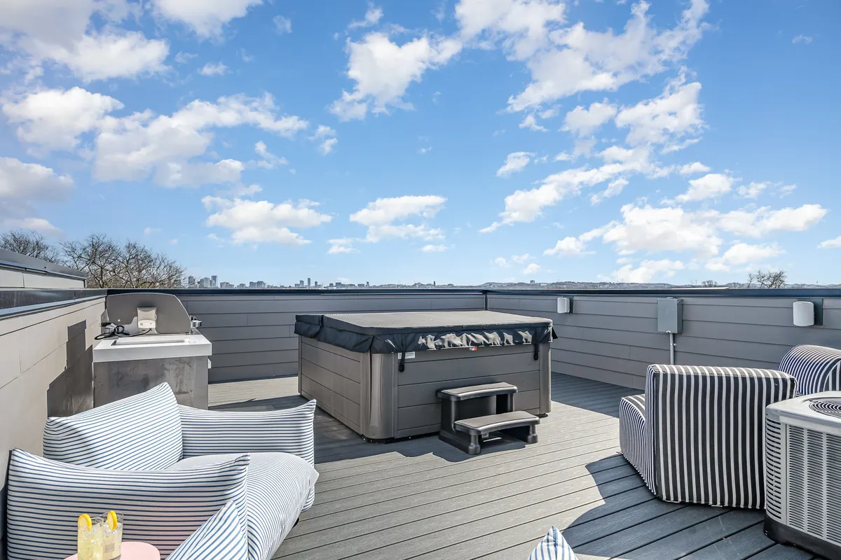 A cozy rooftop setting with striped chairs, a hot tub, and an outdoor grill, all oriented to maximize the views of the surrounding city. The area is perfectly suited for both social gatherings and quiet moments, with inviting seating and lush city vistas.