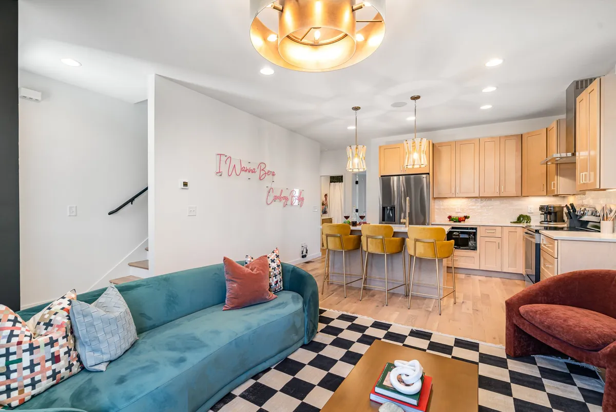 A panoramic view of an open-concept living space that seamlessly connects the plush sofa area, dining space, and modern kitchen. The image highlights stylish decorative wall art, a cozy seating arrangement for gatherings, a kitchen island perfect for preparing meals, and a well-lit, inviting ambiance.