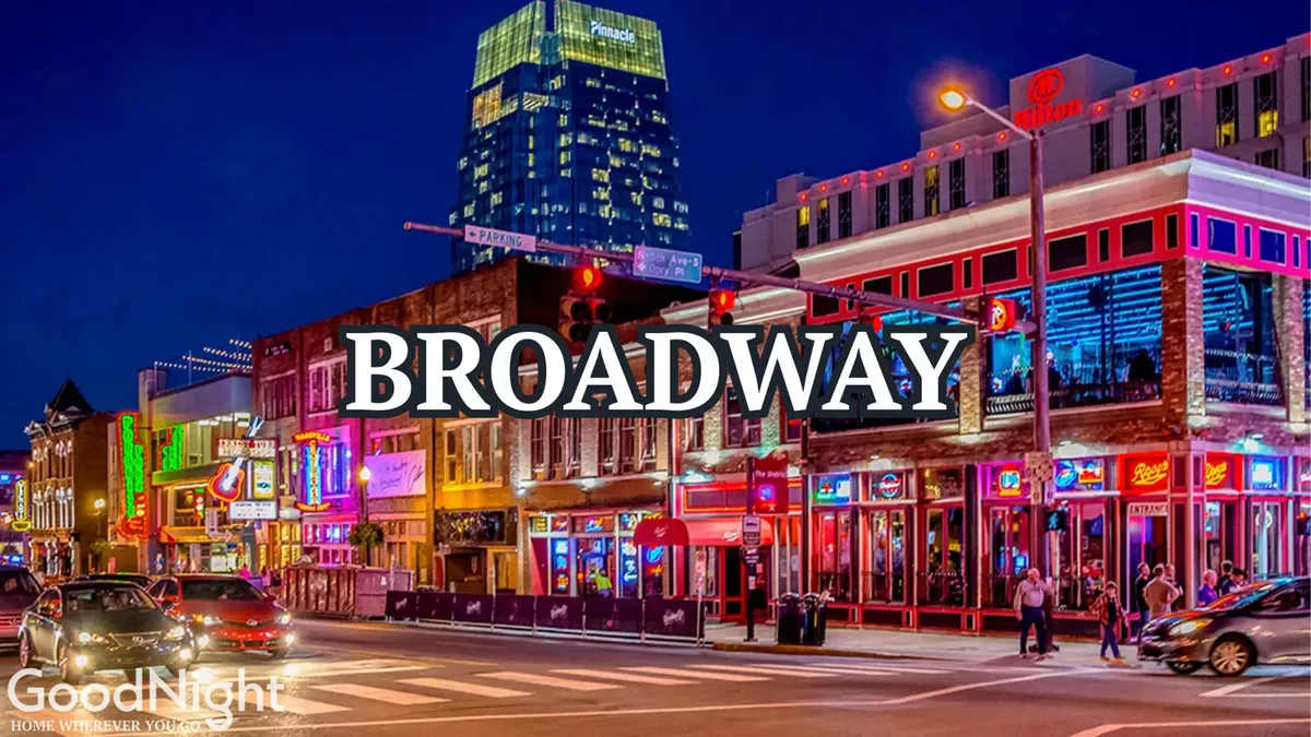 This exterior photo captures Broadway’s iconic neon signs, historic buildings, bustling sidewalks, and a lively nighttime atmosphere. Pedestrians and cars fill the street, adding to the energetic city vibe.